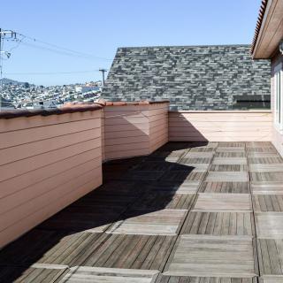 A sunny rooftop terrace with tiled flooring and a view of the skyline.