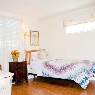 A cozy bedroom with a single bed adorned with a colorful quilt, surrounded by warm lighting and wooden floors.