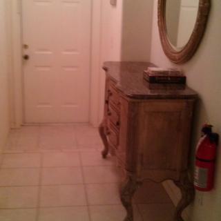 A hallway featuring a decorative console table, wall mirror, and a fire extinguisher near the entrance door.