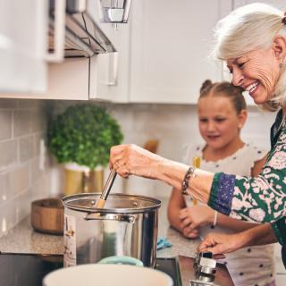 A grandmother and her granddaughter smiling while cooking together in the kitchen.