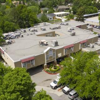 Aerial view of a commercial building surrounded by trees and a parking lot.