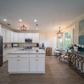 A modern kitchen featuring white cabinets, an island, wood flooring, and a connected dining area with stylish lighting fixtures.