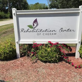A sign for the Rehabilitation Center of Cheban, surrounded by a colorful garden.