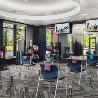 A modern fitness studio with chairs arranged for a class, equipped with exercise balls and mirrored walls.