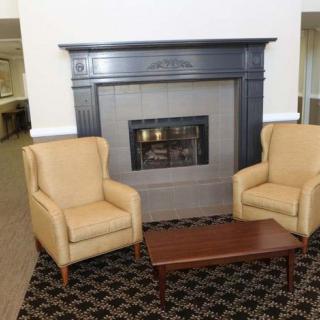 A cozy living room setup featuring a fireplace, two armchairs, and a small coffee table on a patterned carpet.
