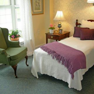 A cozy and inviting bedroom featuring a single bed with a purple throw, a green armchair, and warm lighting.