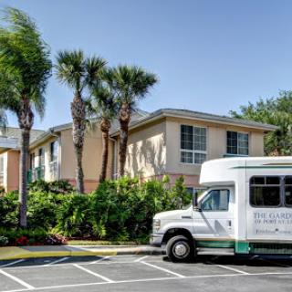A shuttle bus parked in front of a residential building surrounded by palm trees.