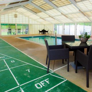 An indoor recreation area featuring a swimming pool and a shuffleboard court with seating.