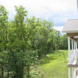 A scenic view of lush green trees near a house with a balcony under a cloudy sky.