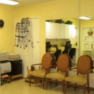 A small waiting area with chairs and a mirror, featuring yellow walls and office equipment.