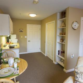 A cozy apartment interior featuring a small dining table, kitchenette, and built-in shelves.
