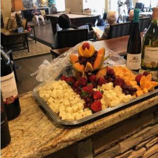 A beautifully arranged fruit and cheese platter accompanied by bottles of wine in a cozy dining setting.