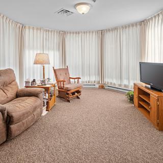 Cozy living room with armchairs, rocking chair, television, and large windows with curtains.