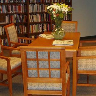 A cozy library corner with a wooden table and chairs, adorned with a vase of fresh flowers.