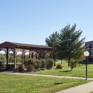 A scenic view of a park featuring a wooden gazebo, surrounding trees, and a well-maintained grassy area under a clear blue sky.
