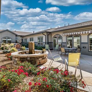 A beautiful outdoor patio area with a fountain, chairs, and vibrant flowers on a sunny day.