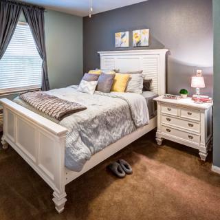 A cozy bedroom with a white bed and nightstand, decorated with pillows and a small lamp.