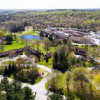 Aerial view of a complex surrounded by trees and roads, featuring buildings and parking areas.