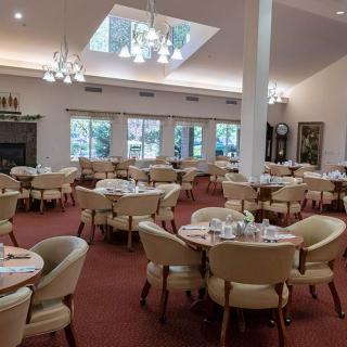 A spacious dining room with elegantly set tables and comfortable chairs, featuring large windows and elegant chandeliers.