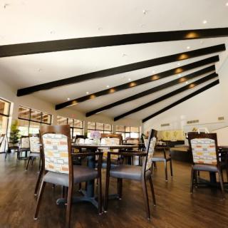 A spacious restaurant interior with wooden flooring, stylish chairs, and tables under a ceiling with exposed beams.