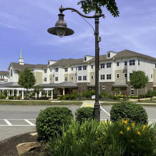 A multi-story residential building with well-maintained landscaping and a decorative lamp post under a clear blue sky.