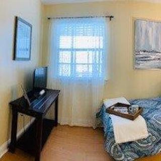 A cozy bedroom with a small desk and computer by the window, and a neatly made bed with a tray.