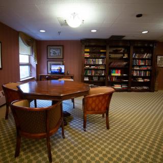A cozy library room with a wooden table, chairs, and bookshelves filled with books.