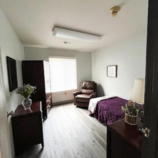 A cozy bedroom featuring a bed, armchair, and natural light coming through the window.