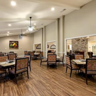 A spacious dining room with elegant tables and chairs, featuring warm lighting and hardwood flooring.