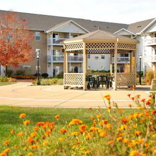 A peaceful park setting featuring a gazebo surrounded by vibrant flowers and residential buildings in the background.