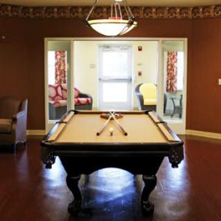 A recreation room featuring a pool table under a chandelier, with seating areas and bright decor.
