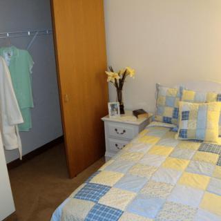 A cozy bedroom with a quilted bedspread, nightstand, and partially open closet.
