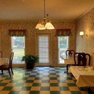 A vintage-style dining room with checkered flooring, decorated with wallpaper and featuring tables and chairs under warm lighting.