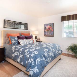 A cozy bedroom with floral bedding and vibrant pillows, featuring artwork and a window for natural light.