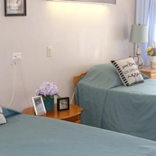 A cozy bedroom with twin beds, featuring decorative pillows and a nightstand adorned with flowers and framed photos.