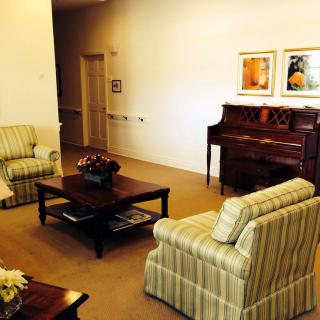 A cozy living room with striped armchairs, a wooden coffee table, and an upright piano against the wall.