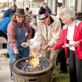 A group of people gathered around a fire pit, enjoying an outdoor cooking activity.