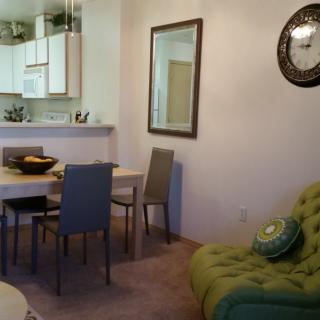 A cozy living and dining area with a green sofa and a wall clock.