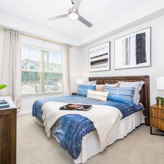 A modern bedroom with stylish decor, featuring a bed with blue bedding, wall art, and a ceiling fan.