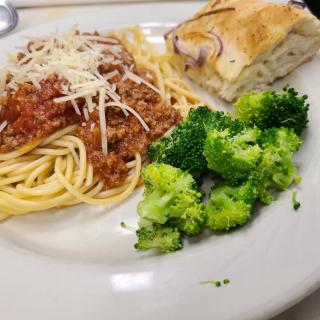 A plate of spaghetti bolognese served with bread and broccoli.