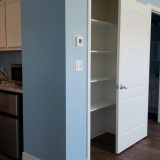 An empty pantry with open shelves next to a kitchen area, featuring a blue wall.