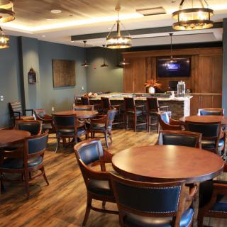 A cozy restaurant interior with wooden tables and chairs, showcasing a bar area and ambient lighting.