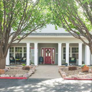 A charming house entrance with a porch and columns, surrounded by trees and landscaping.
