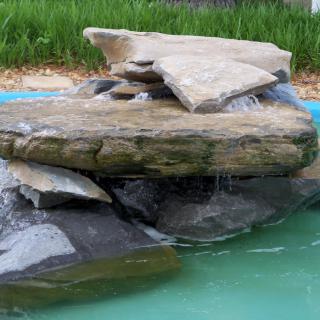 A small waterfall flowing over stacked rocks into a pond.