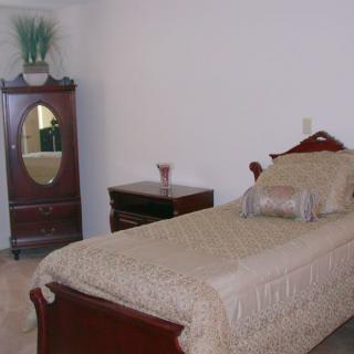 A simple bedroom featuring a single bed with matching furniture, including an armoire and nightstand.