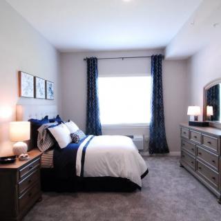 A cozy bedroom with a neatly made bed, dresser, and soft lighting.