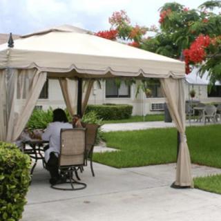 A cozy outdoor gazebo setup with patio furniture, surrounded by a lush garden and lawn.