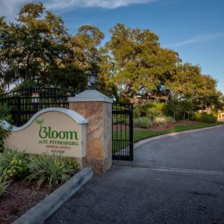 Entrance gate with a sign for Bloom surrounded by lush greenery.