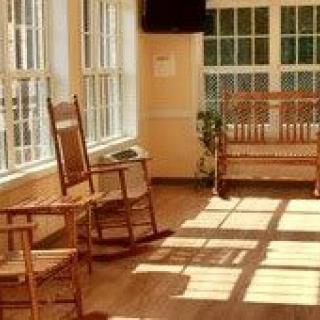 A cozy sunroom with wooden rocking chairs and a bench, illuminated by sunlight streaming through the windows.