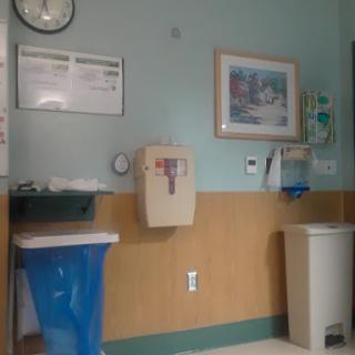 A view of a hospital room featuring a clock, wall art, and various medical waste disposal units.